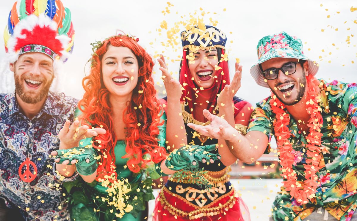 Happy dressed people celebrating at carnival party throwing confetti - Young friends having fun together at fest event - Youth, hangout, festive and happiness concept - Focus on left couple hands