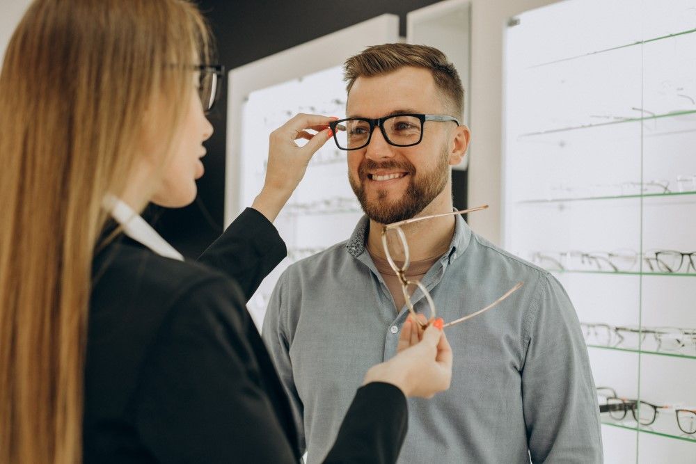 Customer shoosing spectacles at optic store with the lelp of sales person