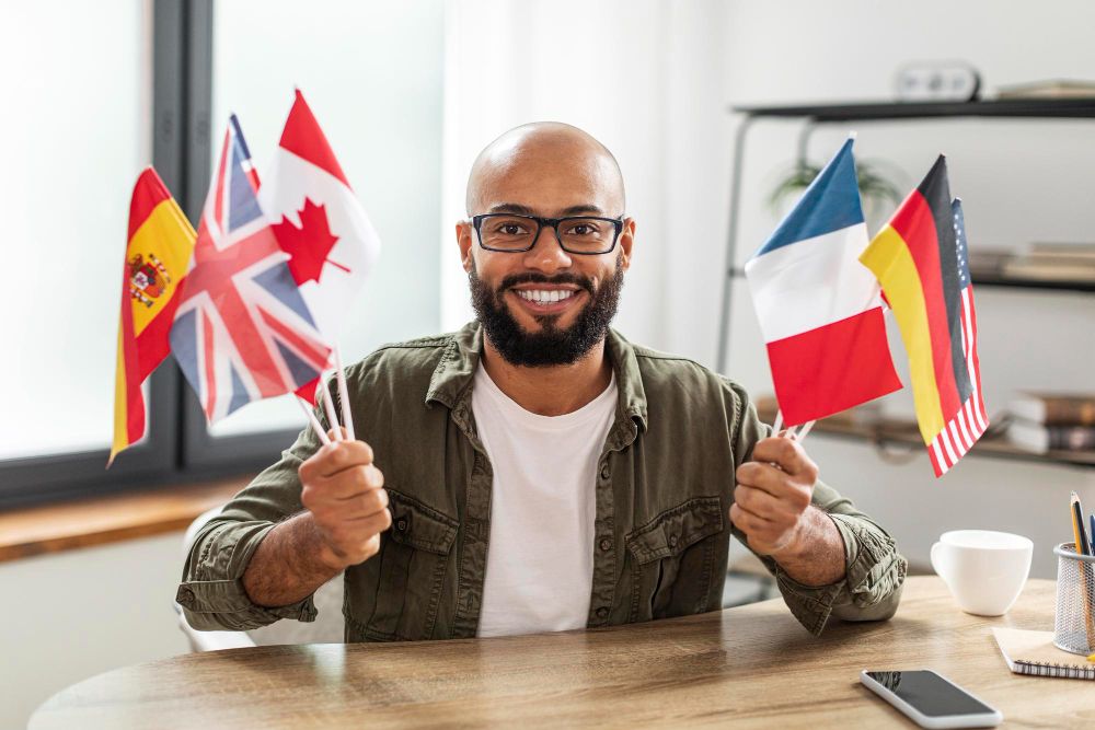 happy-mature-latin-man-studying-at-language-school-online-sitting-at-workdesk-with-flags-of-different-countries