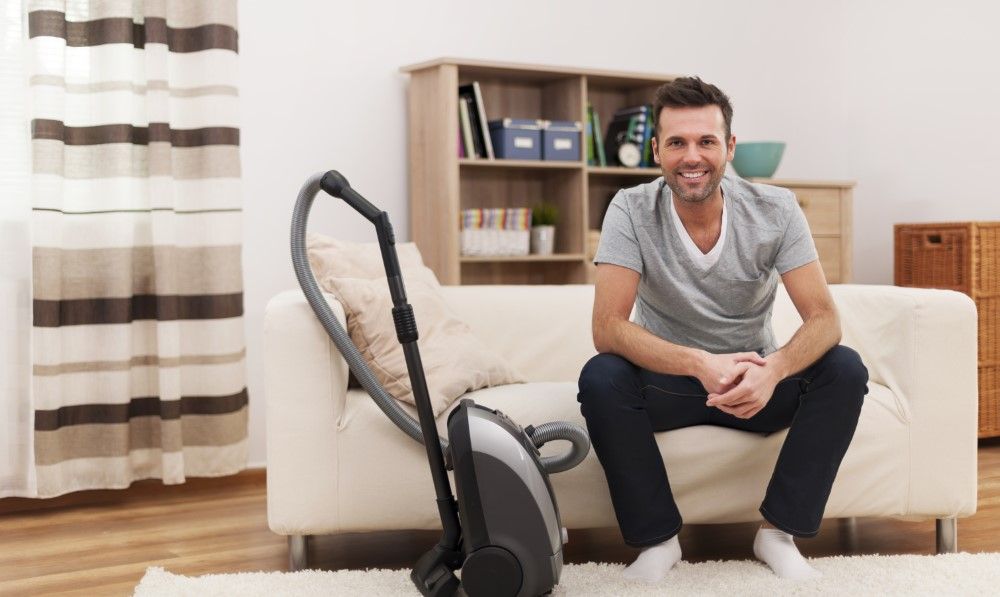 Portrait of smiling man with vacuum cleaner in living room