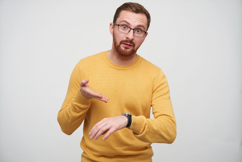 dissatisfied-young-brown-haired-bearded-guy-in-eyewear-pointing-indignantly-on-his-with-wristlet-watch-being-discontented-that-someone-is-late-isolated