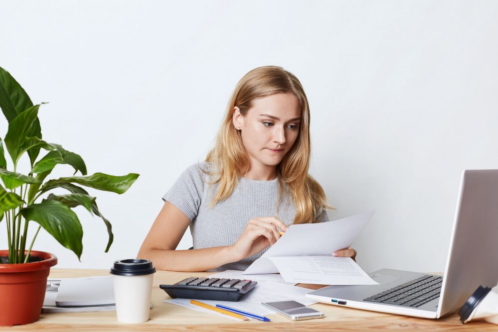 portrait-of-young-businesswoman-working-with-laptop-and-calculator-looking-attentively-at-documents-calcualting-bills-of-company-making-financial-report-people-career-and-business-concept